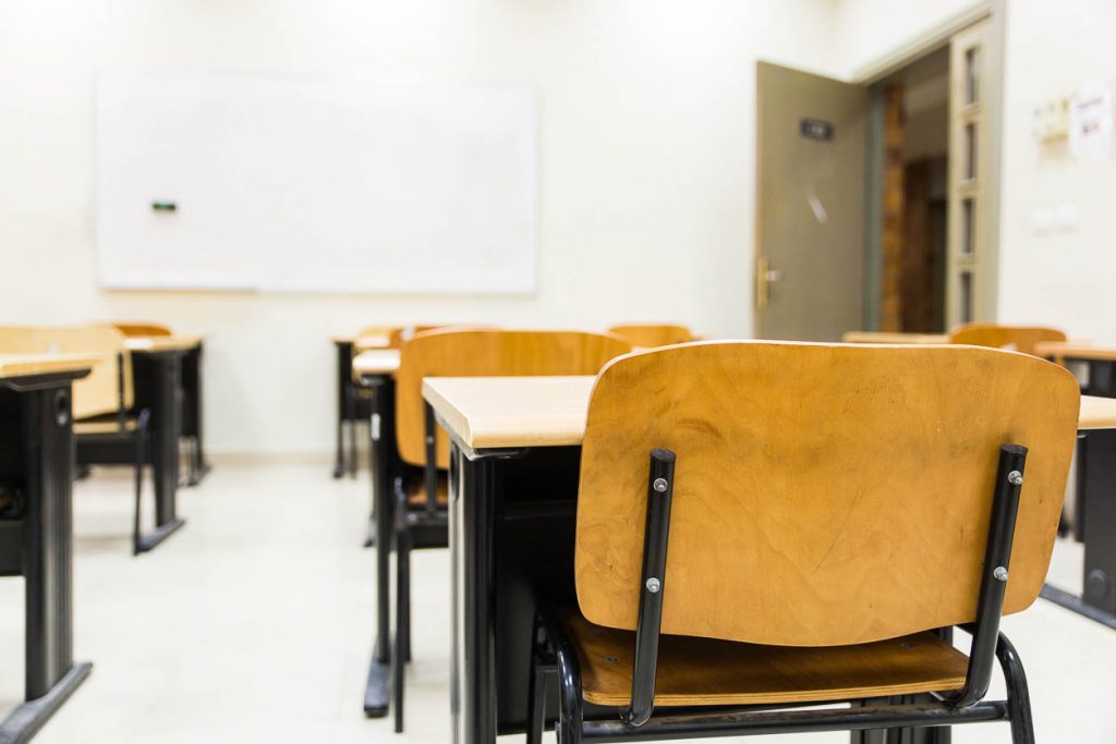 An empty classroom with wooden chairs and desks shot from the back