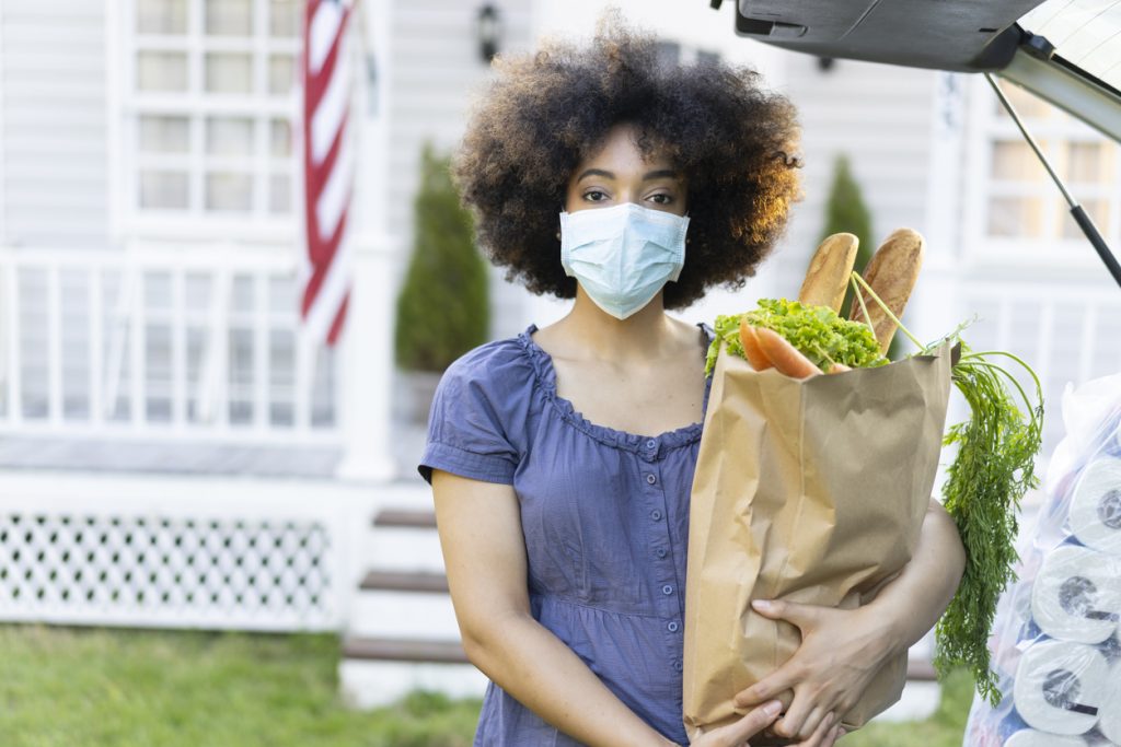 Young afro woman unloads food from the car trunk at the moment of virus pandemic