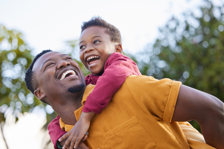 Shot of an adorable little boy enjoying a piggyback ride with his father in a garden